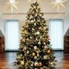 Ozdobený vianočný stromček 3D Smrek Alpsky 240cm zlatými guľami a ozdobami . Pod stromčekom je biela podložka pod vianočný stromček .