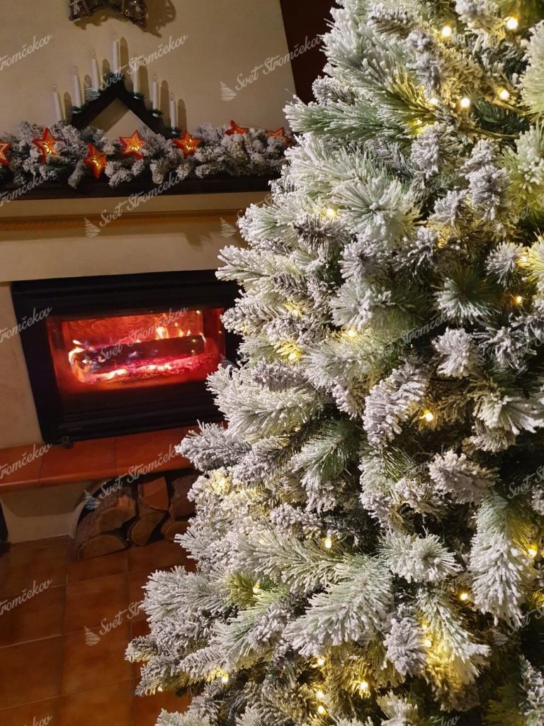 Vianočný stromček Borovica Biela s LED. Detail bieleho vianočného stromčeka so svetielkami pri krbe.