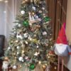 Umelý vianočný stromček 3D Smrek Ľadový 180cm s bielymi a zelenými vianočnými ozdobami a červenou mikulášskou čiapkou vsadený do prúteného košíka miesto stojana
