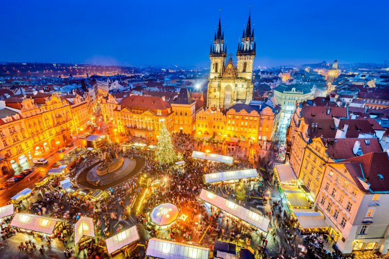 Vysvietené námestie s množstvom ľudí počas vianočných trhov v Prahe.