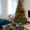 Hustý umelý vianočný stromček s bledozelenými vetvičkami, husto ozdobený medenými ozdobami a teplým bielym osvetlením