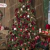 Vysoký a hustý umelý vianočný stromček, s bledozelenými vetvičkami, husto ozdobený červenými ozdobami.