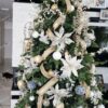 Umelý vianočný stromček so zelenými vetvičkami, ozdobený veľkými bielo-zlatými ozdobami a stuhami, v obývačke.