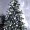 Umelý vianočný stromček so zelenými vetvičkami, ozdobený bielo-striebornými ozdobami a bielym studeným osvetlením.
