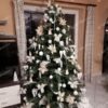 Umelý vianočný stromček so zelenými vetvičkami, ozdobený bielymi ozdobami, v obývačke.