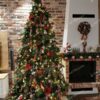 Vysoký umelý vianočný stromček so zelenými vetvičkami so zabudovaným LED osvetlením, husto ozdobený červeno-zelenými ozdobami, pri krbe v obývačke.