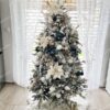 Zasnežený umelý vianočný stromček s husto zasneženými vetvičkami, husto ozdobený bielo-zlatými ozdobami, s bielym kobercom pod stromček.