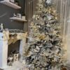 Husto ozdobený umelý vianočný stromček so zasneženými vetvičkami, s bielo-zlatými ozdobami, s bielym koberčekom pod stromček, pri krbe v obývačke.