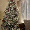 Umelý vianočný stromček so zasneženými vetvičkami, ozdobený červeno-zlatými ozdobami a teplým bielym osvetlením, v obývačke