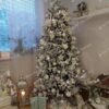 Biely umelý vianočný stromček s husto zasneženými vetvičkami,husto ozdobený bielymi ozdobami a bielym osvetlením.