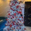Vysoký umelý vianočný stromček so zasneženými vetvičkami, s červenými ozdobami a bielym osvetlením.