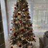 Umelý vysoký zasnežený vianočný stromček s červeno-bielymi ozdobami a s teplým bielym osvetelením.