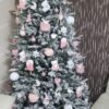 Vysoký umelý vianočný stromček so zasneženými vetvičkami, ozdobený ružovo-bielymi ozdobami.