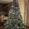 Vysoký a široký umelý vianočný stromček, husto ozdobený červeno-zlatými ozdobami a teplým bielym osvetlením.