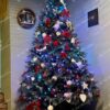 Vysoký a široký umelý vianočný stromček s bledými končekmi vetvičiek, ozdobený bielo-červenými vianočnými ozdobami v rohu obývačky.
