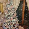 Zasnežený vysoký umelý vianočný stromček s bielo-ružovými ozdobami.