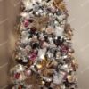 Úzky zasnežený vianočný stromček s bielo-ružovými ozdobami a zlatými vianočnými ružami.