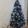 Umelý vianočný stromček ozdobený drevenými a bielymi ozdobami, s bielym koberčekom pod stromček.