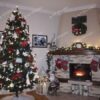 Umelý vianočný stromček so zasneženými koncami vetvičiek s bielo-červenými vianočnými ozdobami, pri krbe v obývačke