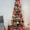 Úzky umelý vianočný stromček so zasneženými vetvičkami, červeno-zlatými ozdobami a teplým bielym osvetlením.
