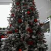 Zasnežený umelý vianočný stromček čeveno-bielymi vianočnými ozdobami