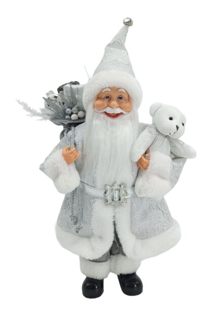 Dekorácia Santa Claus strieborný 40cm je oblečený v striebornom kabátiku s bielym lemom. Opásaný je strieborným opaskom. Na nohách má obuté čierne topánky. Má hustú bielu bradu a okuliare. v ruke drží bieleho plyšového medveďa ana pleci má zavesný batoh s darčekmi.
