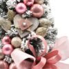 Zasnežený malý vianočný stromček s ružovými vianočnými guľami a mašľou.