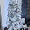 Umelý vianočný stromček Borovica Biela Úzka 225cm, stromček má husto zasnežené vetvičky a je ozdobený striebornými a čiernymi ozdobami